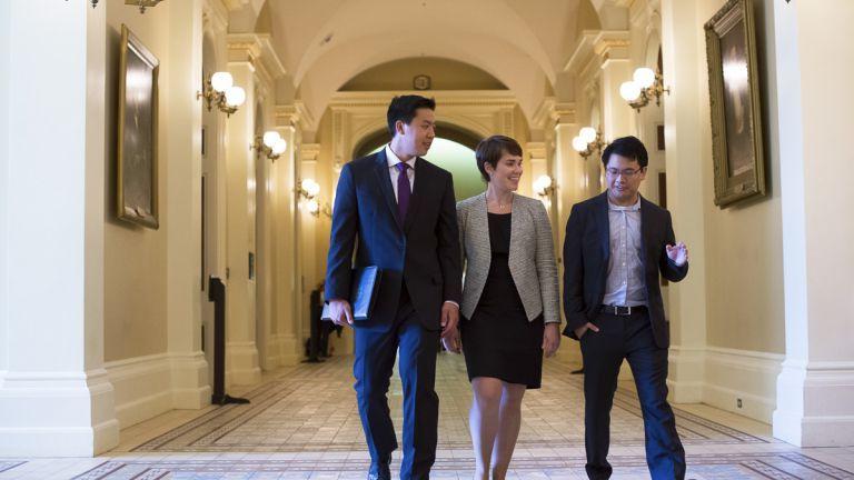 Three students dressed in suits walk through a hallway of the California State Capitol.