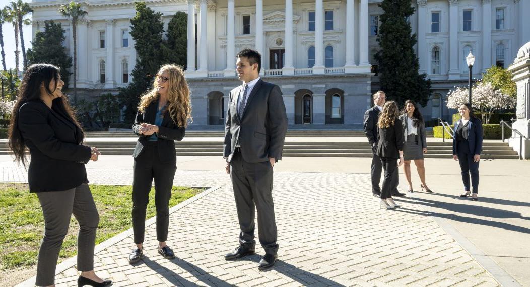 Two small groups of people in suits chat with each other in front of the Capitol Building 